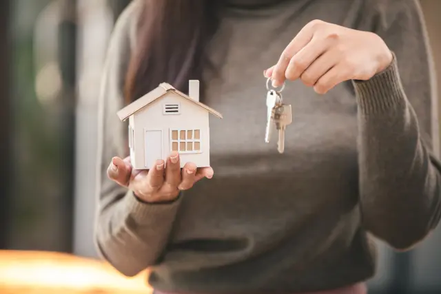 A person holding a model house in one hand and a bunch of keys in the other.